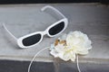 Sunglasses, a white flower and the bride and groom\'s rings lie on a gray concrete surface. Wedding accessories