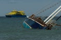 Sunken sail boat in front of a bright yellow passanger ferry in stormy weather in the Western Caribbean