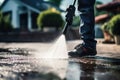 Sunlight breaks through as a man in work boots and jeans uses a pressure washer on a driveway.