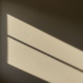 Sunlight creates sharp, angular shadows on a textured beige wall. The shadows form Royalty Free Stock Photo
