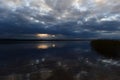 Sunlight from dark clouds at sunset reflects on the lake water