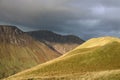 Sunlight on grassy mountain ridge, dark clouds