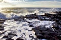 Sunlight highlighting waves crashing onto the hexagonal Basalt slabs of Giants Causeway