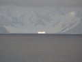 Sunlight picks out a lone iceberg before mountains in Antarctica