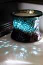 Sunlight reflecting off turquoise and brown crackled glass candle on ivory marble bathroom vanity