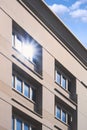 Sunlight reflection on surface of multiple blue glass windows on gray office building wall against white cloud and blue sky Royalty Free Stock Photo