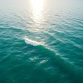 Sunlight reflects off a calm, expansive ocean surface, creating a glittering effect. The