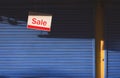 Hanging sale sign board in front of blue automatic shutter door of shop house