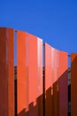 Sunlight and shadow on surface of orange curved steel wall decoration outside of high building against blue clear sky