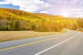 Sunlight shines above empty highway road through colorful fall forest