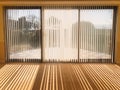 Sunlight shining through full length white vertical blinds in front of three glass sliding french doors leading to a patio.