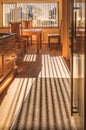 Sunlight shining into a kitchen through vertical blinds casting a long striped shadow on the wooden floor