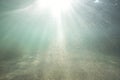 Sunlight shining through the ocean surface and reaching the sea bed as sand is dragged up by the current