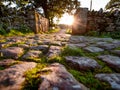 Sunlight shining through an old stone gate illuminating a moss-covered cobblestone path surrounded by rustic weathered walls and Royalty Free Stock Photo