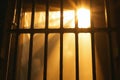 Sunlight streams through prison bars, casting dramatic shadows in a dim jail cell setting Royalty Free Stock Photo