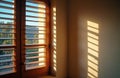 Sunlight streams through wooden window shutters creating distinct shadow stripes on wall. Warm golden light falls on interior Royalty Free Stock Photo