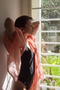 Sunlit freckled woman, wearing underwear and a pink pashmina scarf, holding her nape Royalty Free Stock Photo