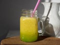 Sunlit glass jar with yellow smoothies. There`s a drinking tube in the jar. Wooden background
