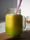 Sunlit glass jar with yellow smoothies. There`s a drinking tube in the jar. Wooden background. Vertical photo