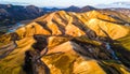 Sunlit mountain range with colorful slopes and a winding river from an aerial viewpoint Royalty Free Stock Photo