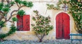 Sunlit old wall with red wooden door and balcony with roses and climbing plants. Royalty Free Stock Photo