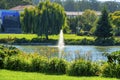 Sunlit park with grass shrubs and decorative trees pond or lake and powerful water spout in center of water afternoon Royalty Free Stock Photo