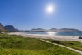 Sunlit pathway meandering through grass and wildflowers to the white sands of Rambergstranda Beach in Jusnesvika Bay, Lofoten Royalty Free Stock Photo