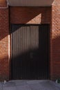 Sunlit red brick wall with dark wooden double leaved door and diagonal hard shadow Royalty Free Stock Photo