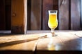 sunlit saison beer glass casting a shadow on a wooden table