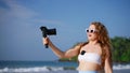 Travel influencer records beach vlog with pro camera, wireless lav mic. Sunlit tropical backdrop, engaging viewers, solo