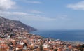 Sunlit view of the city of funchal from above with rooftops and buildings in front of a bright blue sea