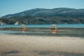 Sunlougers below umbrellas in the shallow water of turquoise bay. Opposite mountainous island with windmills on the top