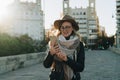 Sunny autumn day, backlight. Young attractive woman travels in hat and eyeglasses stands on city street, uses smartphone Royalty Free Stock Photo