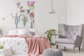 A sunny bedroom interior with a bed dressed in green pattern white linen and a peach blanket. Gray comfortable armchair beside the Royalty Free Stock Photo