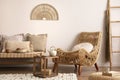 Sunny and bright composition of meditation living room interior with armchair, beige carpet, pillows, ornament and personal