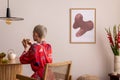 Sunny and bright space of living room with mock up poster frame, woman in red kimono, bouquet flower in vase and personal Royalty Free Stock Photo