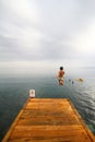On a sunny and cloudy day in the Aegean Sea, children are having fun jumping into the sea from the pier.