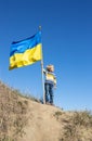 on sunny day, boy stands on hill against blue sky, holding large waving blue and yellow national flag Royalty Free Stock Photo