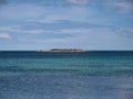 On a sunny day with calm, turquoise waters and a blue sky, the rocky outcrop of Black Skerry off the island of Yell in Shetland