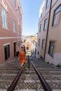 A Sunny Day in Lisbon: Vertical Shot of a Young Woman in a Bright Orange Dress Descending a Steep, Cobblestone Street, Holding