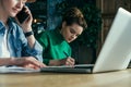 Sunny day. Two young business women sitting in office at table and work together.On table laptop and paper charts. Royalty Free Stock Photo