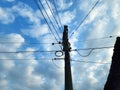 a sunny day with white clouds and an electric pole with a very long cable