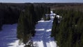 Sunny day in winter forest. Clip. Aerial view of a long road on snow covered ground among green trees. Royalty Free Stock Photo