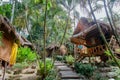 Sunny forest with wooden bungalows in lush of tropic island. Jungle houses for tourists and locals in South-Eastern Asia