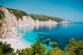 Sunny Fteri beach lagoon with rocky coastline, Kefalonia, Greece. Tourists under umbrella chill relax near clear blue