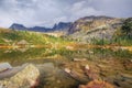 Sunny Lake Raduzhnoe in front of rocks among taiga and large stones under storm clouds in Ergaki