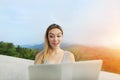 Sunny light portrait of blonde girl using laptop, mountains in background, Bali.