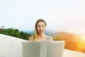 Sunny light portrait of young girl using laptop, mountains in background, Thailand.