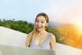 Sunny light portrait of young smiling girl using laptop, mountains in background, Thailand.