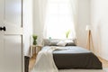 Sunny natural style bedroom interior with a bed in the middle, gray linen and pillows, and a vanilla blanket. A lamp and a stool w